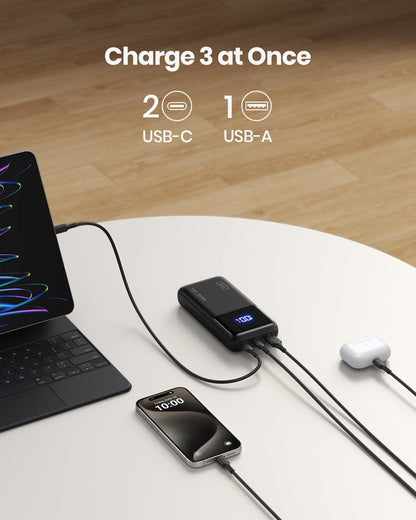 INIU B62 power bank charging three devices simultaneously: MacBook, iPhone, and AirPods. Features 2 USB-C and 1 USB-A port.